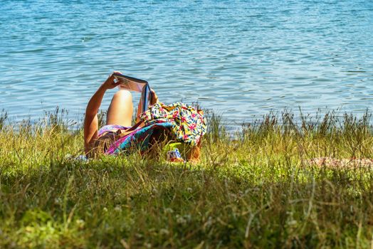 A girl lies in a river and reads a book. Young woman reading a book sitting by the river.