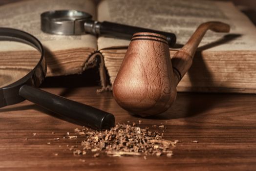 Wooden pipe with smoke on heap of chopped dried tobacco leaves against black background.