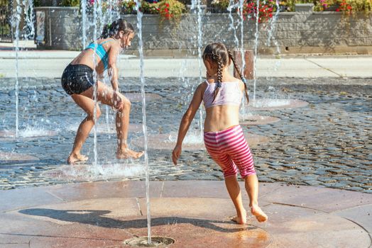 Children on a sunny summer day are poured water from a fountain.Children happily in shallow clean water on of city fountain on warm bright summer day.