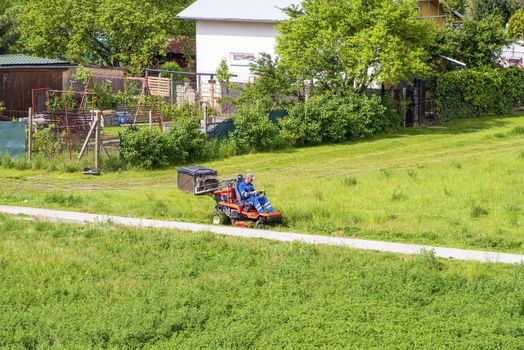 Worker mowing grass in city park. Sunny summer day.Mature man driving grass cutter in a sunny day.Gardener driving a riding lawn mower in a garden