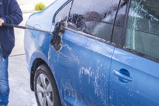 Manual car wash with pressurized water in car wash outside.Using a brush to wash a car on a car washing facility on sunny summer day.Blue car manual wash of with pressurized water in car wash outside.