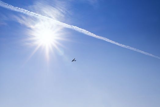 Blue sky . Against the background of blue sky and bright sun, an airplane is flying. Basic background for design.Aircraft flying in the sky against a background of a bright sunset.