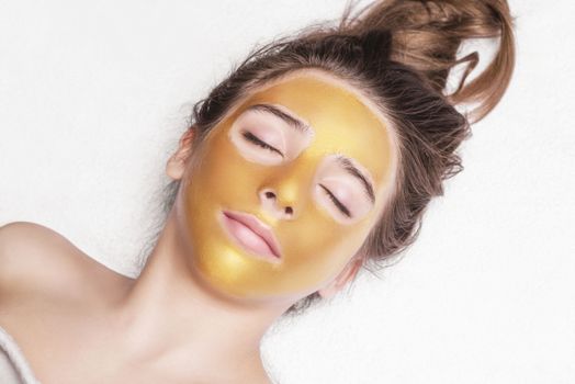 Beautiful girl with a cosmetic mask on the face of golden color. Beautiful model removing golden facial skin cosmetic. Beauty skincare .Close-up. Free space. Woman gold mask. .