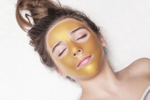 Beautiful girl with a cosmetic mask on the face of golden color. Beautiful model removing golden facial skin cosmetic. Beauty skincare .Close-up. Free space. Woman gold mask. .