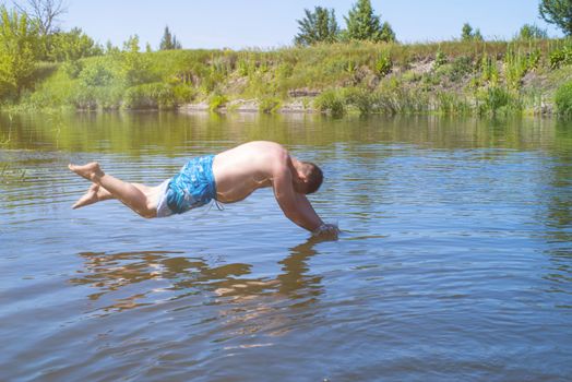 ?an jumps like fish into the water of the lake, swims, enjoys spending time on summer holidaysA fat man jumping on a summer day into a river with a run up.