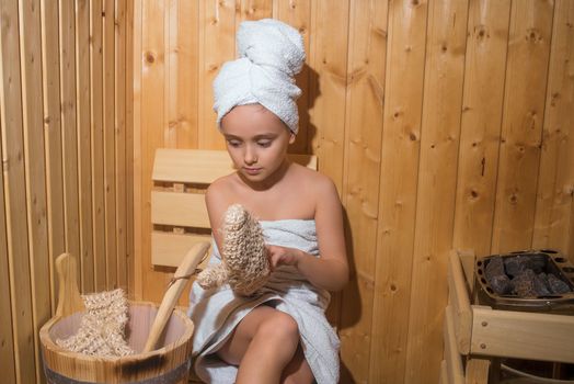 Young Girl relaxing in sauna,girl in a spa treatment in a traditional sauna with a brush for skin and a washcloth.Girl enjoying a relaxing stay in the sauna.