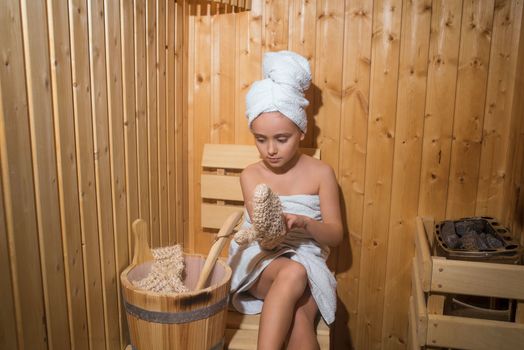 Young Girl relaxing in sauna,girl in a spa treatment in a traditional sauna with a brush for skin and a washcloth.Girl enjoying a relaxing stay in the sauna.