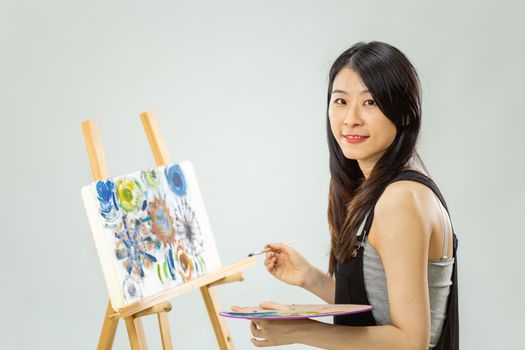 Artist painting on an easel, looking at camera