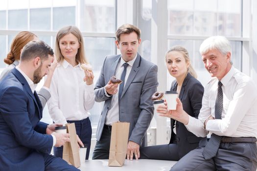 Business people having coffee break eating donuts together in office