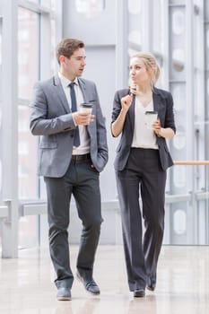 Businessman and businesswoman walk together and talk about business holding coffee in hand