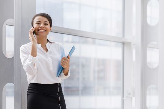 Happy african businesswoman smiling and talking on the phone, holding folder of documents
