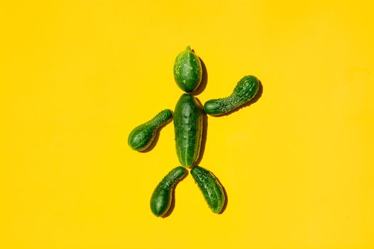 Cucumber man on a yellow background. Figure of man made from cucumbers. Copy space. Cucumbers for designers. Top view. Cucumber harvest. Farming, gardening, agriculture, harvesting and people concept.