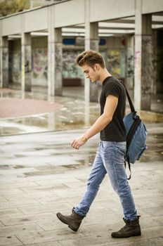 Attractive young man wearing black T-shirt and jeans with backpack walking outside
