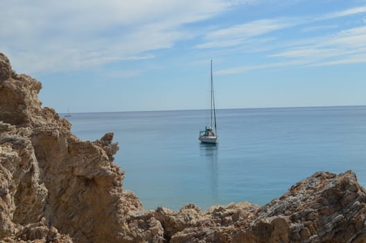 Sailboat in The Mediterranean Sea In Calm Water With a Rock in The Fore Ground