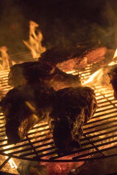 Grilling steaks on a barbecue with open flames on a wood fire
