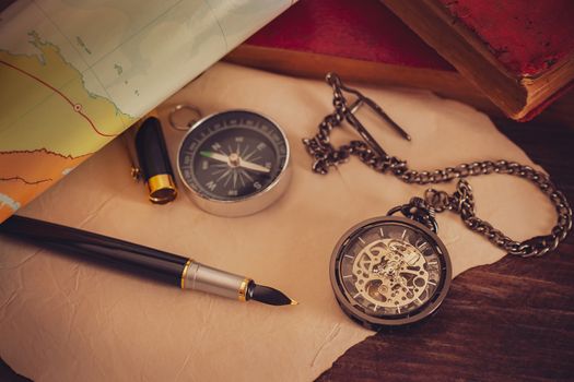 Pocket watch with old books and pen with paper map on the table by the window. Concept of travel planning.