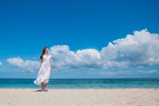 Young woman in white dress walking along sand tropical beach