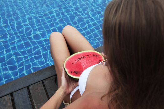 Beautiful woman with fit, tanned body in bikini with watermelon tanning poolside