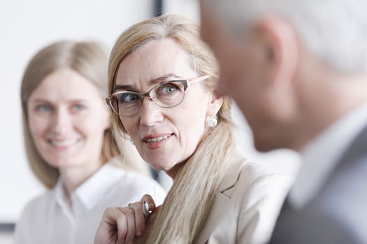 Business people sitting in a row and working, focus on mature woman in glasses