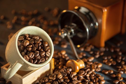 Coffee bean in the white cup and coffee grinder on wooden table. Concept breakfast or coffee time in morning.