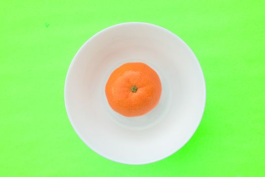 One mandarin orange in a white bowl looks like an egg with the egg yolk, creative photo