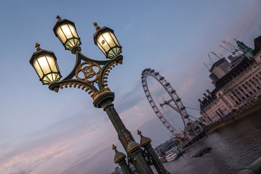 View of the London Eye with the City Hall of London from the Westminster bridge with a nice street light after sunset