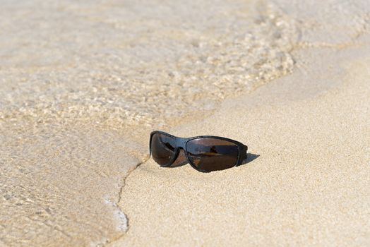 Black sunglass left in the sand on the beach 