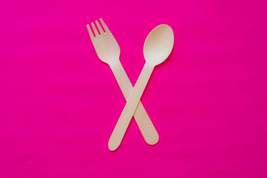 Wooden fork and spoon on a strong pink colour background, concept studio photo