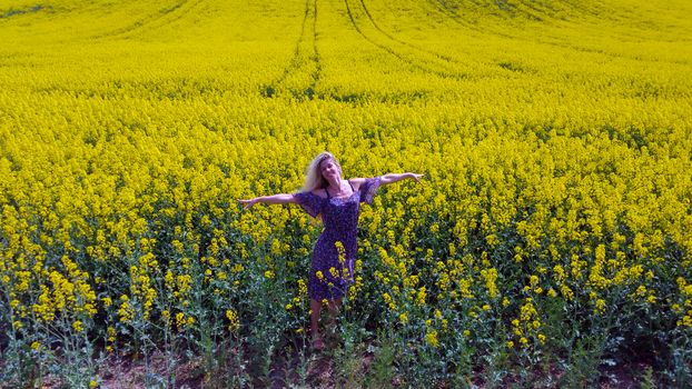 happy blonde girl in dress with flower print on the blooming yellow rapeseed field