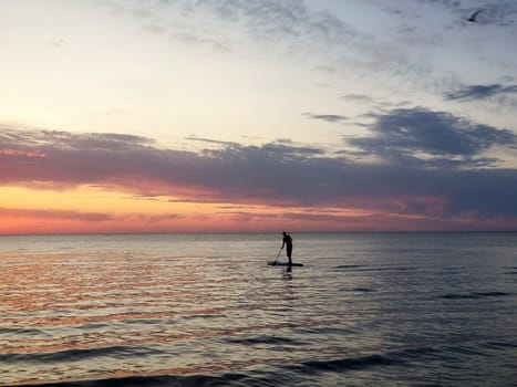 silhouette of a man on the SUP ,Stand Up Paddle board, against the background of the colored sunset at sea.