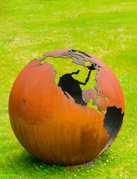 Large iron, rusty globe stands on a clearing in the grass
