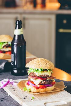 Cheeseburger with Two Beef Patties, Cheddar Cheese, Bacon, Iceberg Lettuce, Sliced Tomatoes and Red Onion. Bottle of Beer and Some Ingredients on Table.
