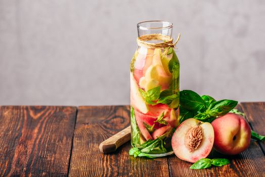 Bottle of Summer Water with Sliced Peach and Basil Leaves. Knife and Ingredients on Wooden Table.