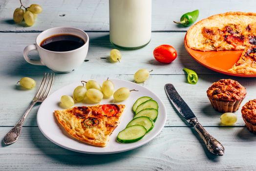 Breakfast frittata with chorizo, tomatoes and chili peppers on plate with cup of coffee, grapes and muffins over light wooden background. Healthy eating concept.