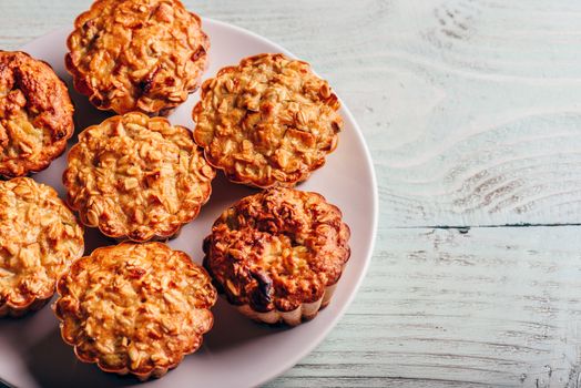 Cooked oatmeal muffins on white plate over light wooden background.