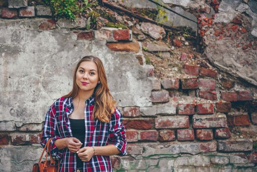 Beautiful girl is looking at camera and standing against brick wall