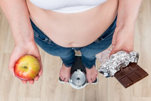 woman on scales makes the choice between apple and chocolate concept photo slimming and healthy eating