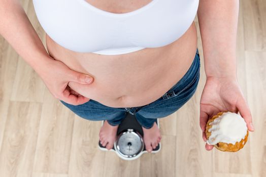 fat woman with donut standing on the scales, concept photo nutrition and healthy lifestyle