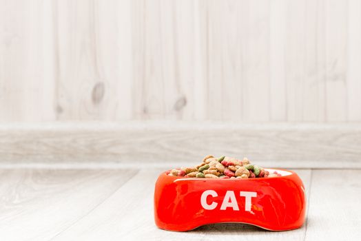 Red bowl for a cat with dry food on the floor in the house close-up