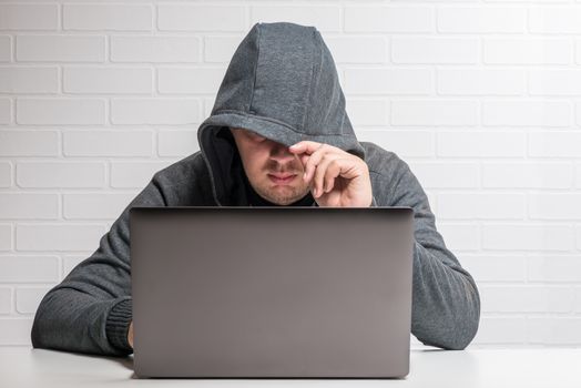 A hacker in a hood with a laptop steals data and distributes a virus