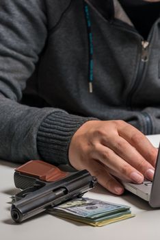 close-up of a hacker's hand with money and a gun with a laptop