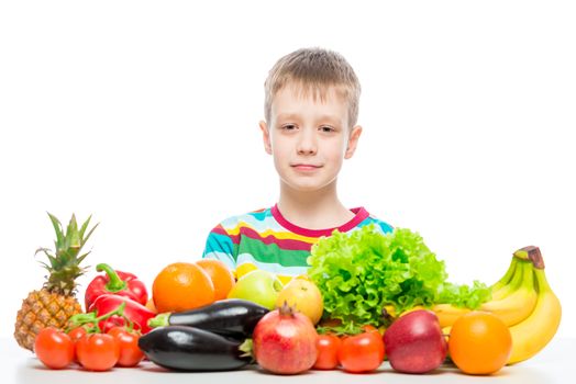 Portrait of a boy at the table with a pile of fresh vegetables and fruits isolated in studio