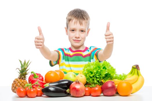 Happy boy at the table with a pile of fresh vegetables and fruits isolated in studio