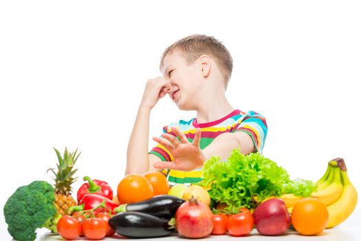 Concept photo of an unloved food - portrait of a boy with an aversion to vegetables and fruits on a white background