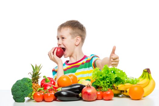 Happy boy on a diet with food, eating a red apple sitting at the table