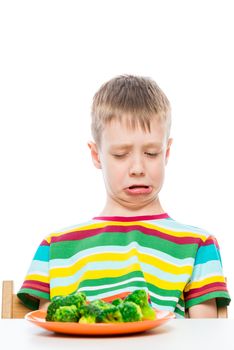 boy with disgust looks at a plate of broccoli, portrait on white background isolated