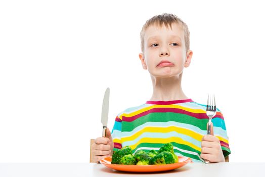 Boy disgusted with eating broccoli, portrait isolated on white background