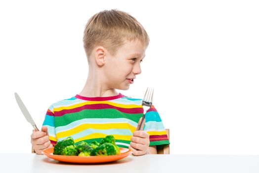 portrait of a boy with a plate of tasteless broccoli on a white background