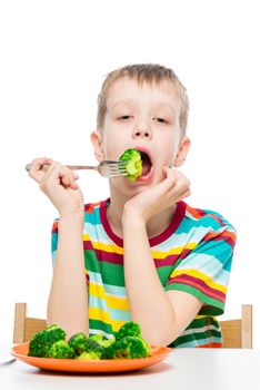 Vertical portrait of a boy who has a diet food, a child eats broccoli on a white background
