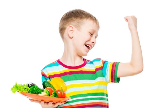 a boy with a plate of fresh vegetables shows his muscles from wholesome food, the portrait is isolated